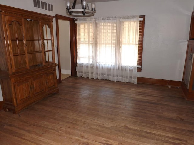 unfurnished dining area with an inviting chandelier, baseboards, dark wood-style floors, and visible vents