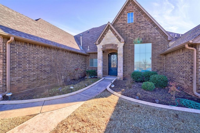 view of exterior entry featuring stone siding, a shingled roof, and brick siding