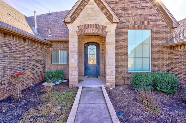 entrance to property featuring a shingled roof, stone siding, and brick siding