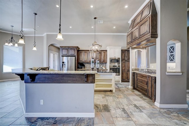 kitchen with arched walkways, a large island, hanging light fixtures, backsplash, and appliances with stainless steel finishes