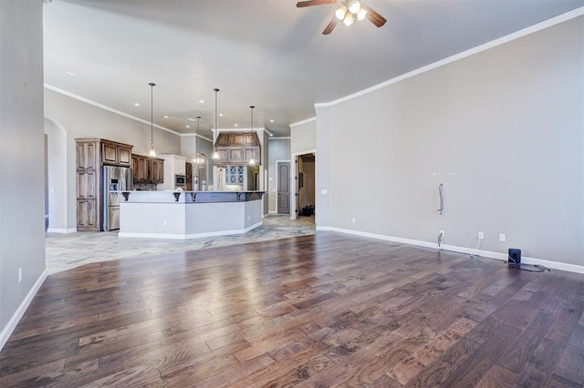 unfurnished living room with arched walkways, ceiling fan, dark wood-style flooring, baseboards, and ornamental molding