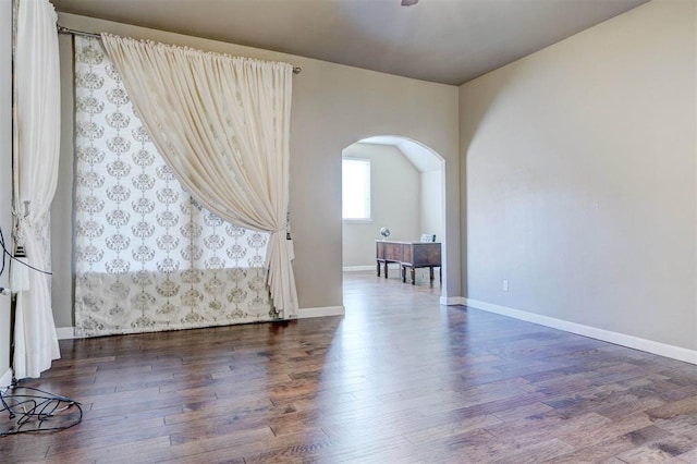 spare room with arched walkways, dark wood-style flooring, and baseboards