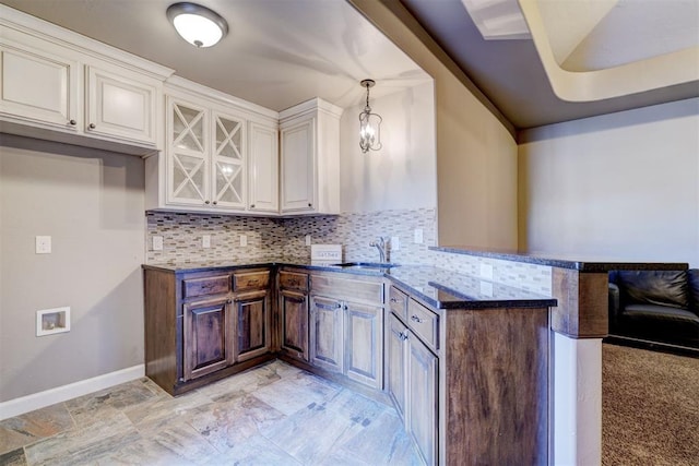 kitchen featuring backsplash, white cabinetry, a sink, a peninsula, and baseboards