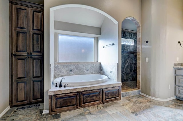 bathroom with a bath, walk in shower, vanity, and baseboards