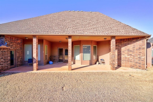 back of property with brick siding, roof with shingles, and a patio area