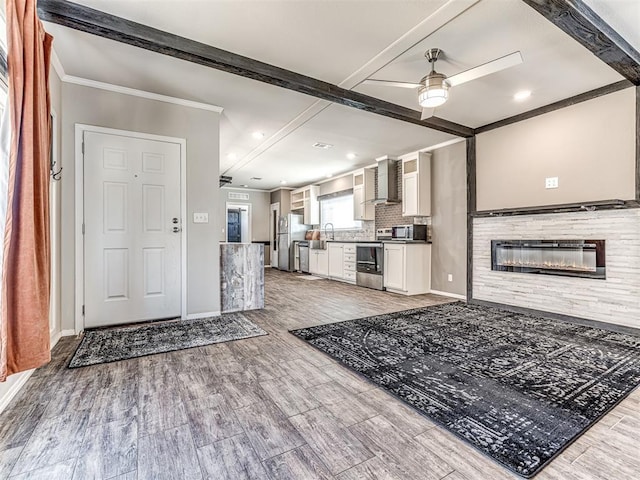 kitchen featuring stainless steel appliances, a sink, light wood-type flooring, wall chimney exhaust hood, and dark countertops