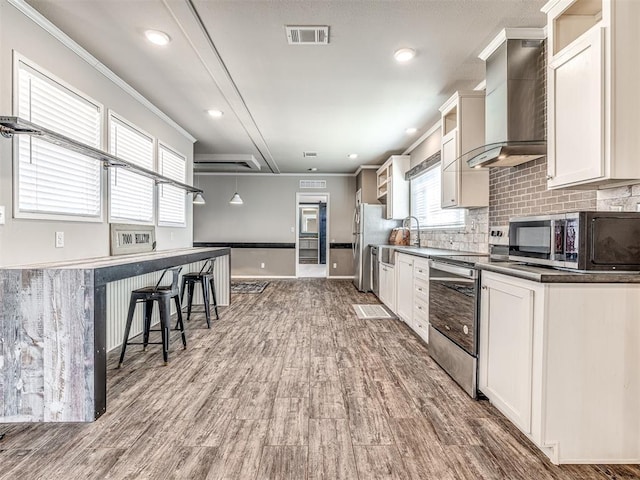 kitchen featuring visible vents, dark countertops, stainless steel appliances, wall chimney range hood, and white cabinetry