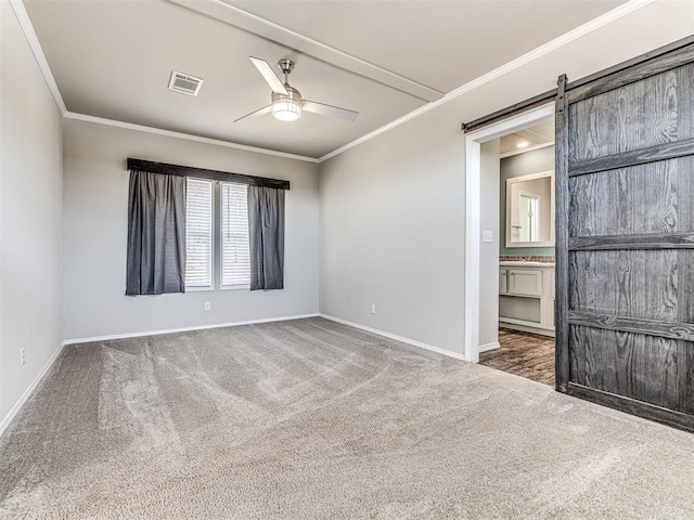 unfurnished bedroom featuring dark colored carpet, crown molding, baseboards, and a barn door