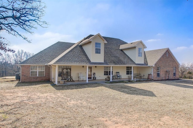 view of front facade featuring a shingled roof, cooling unit, brick siding, and a patio