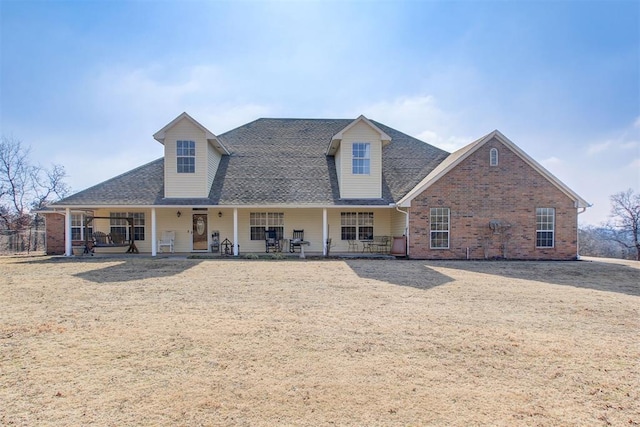 back of property with covered porch, brick siding, and roof with shingles