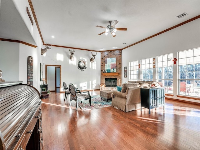 living room with visible vents, a ceiling fan, ornamental molding, a brick fireplace, and wood finished floors