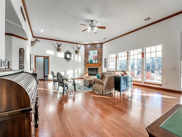 living room with visible vents, a ceiling fan, light wood-style flooring, ornamental molding, and a brick fireplace