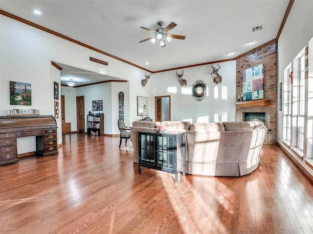 living area with crown molding, visible vents, a ceiling fan, a brick fireplace, and wood finished floors