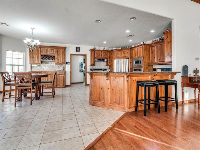 kitchen with tasteful backsplash, brown cabinetry, dark stone countertops, a peninsula, and stainless steel appliances