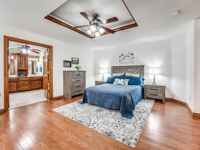 bedroom featuring light wood-style floors, a raised ceiling, connected bathroom, and baseboards