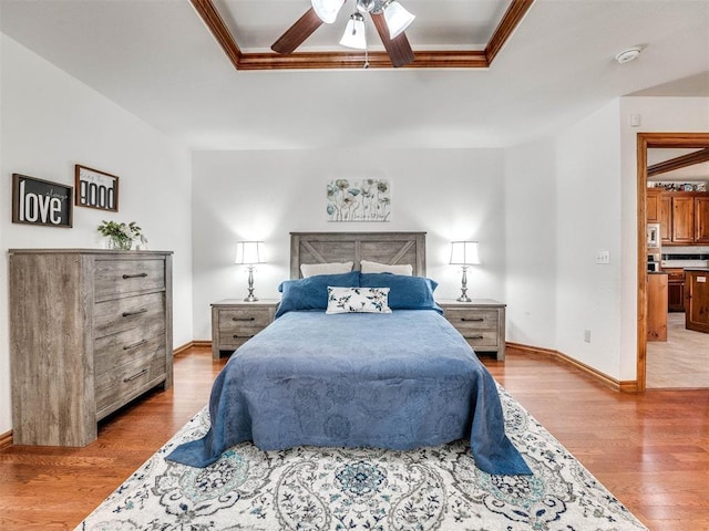 bedroom featuring light wood-type flooring, baseboards, a tray ceiling, and crown molding