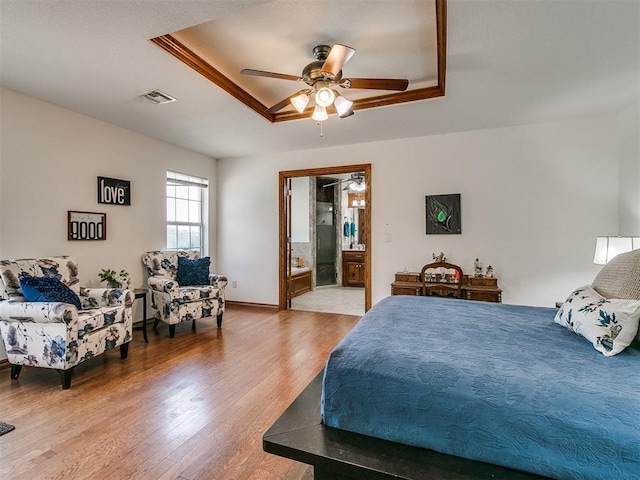 bedroom with a tray ceiling, ensuite bath, wood finished floors, and visible vents