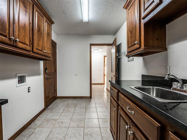 kitchen with light tile patterned floors, baseboards, dark countertops, a textured ceiling, and a sink