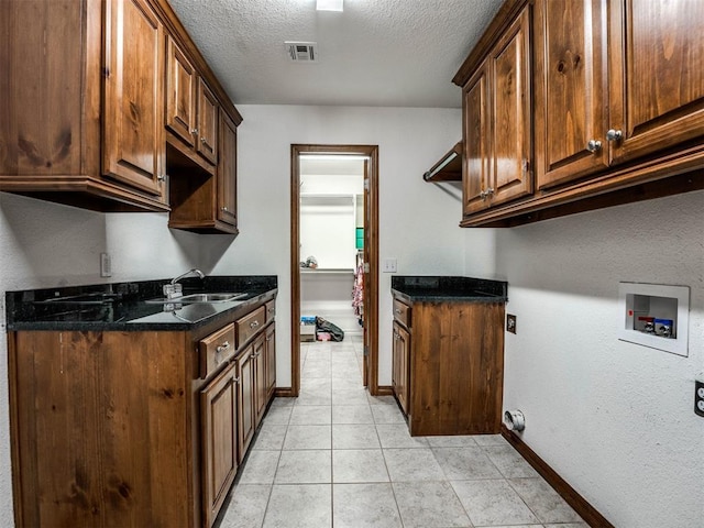 kitchen featuring light tile patterned floors, visible vents, a sink, a textured ceiling, and dark stone counters