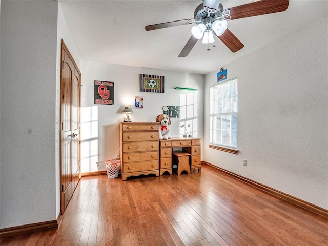 office area with ceiling fan, a textured wall, wood finished floors, and baseboards