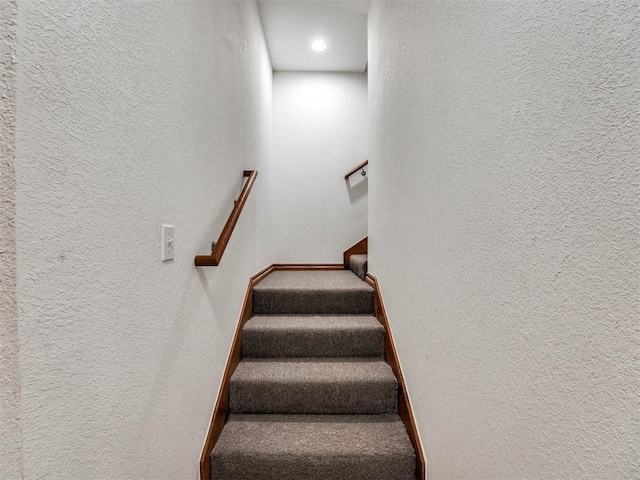 staircase featuring a textured wall, carpet floors, and baseboards