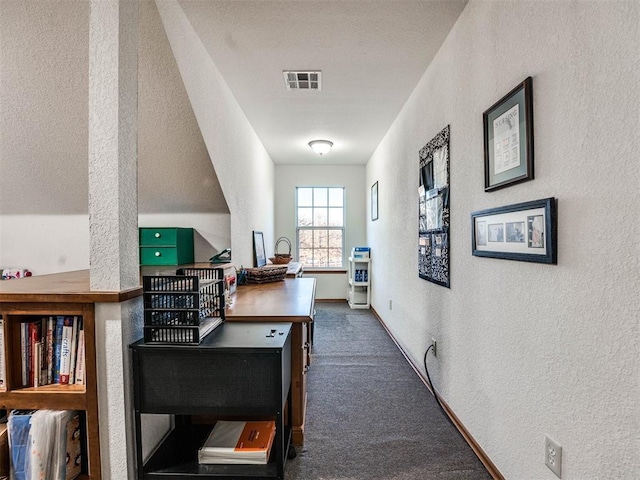 hall with baseboards, visible vents, dark colored carpet, and a textured wall