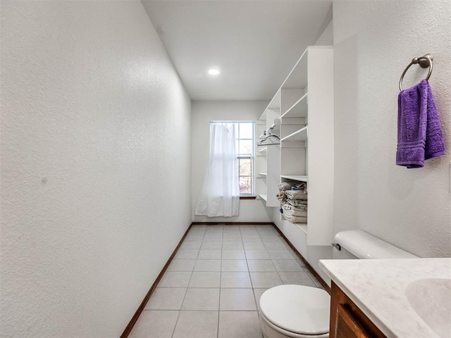 full bathroom featuring a textured wall, toilet, vanity, baseboards, and tile patterned floors