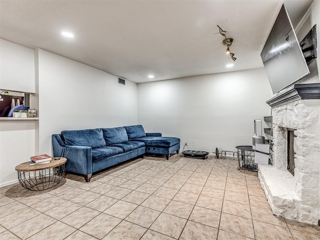 living area with light tile patterned floors, a stone fireplace, recessed lighting, visible vents, and rail lighting