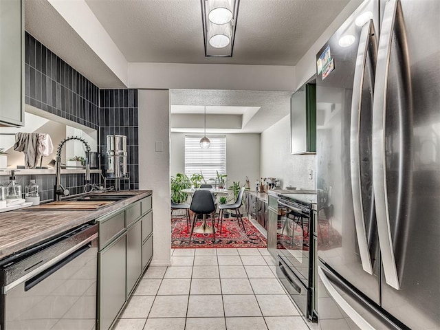 kitchen featuring light tile patterned floors, a raised ceiling, appliances with stainless steel finishes, a sink, and a textured ceiling