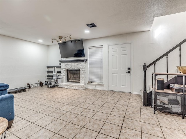 living room featuring light tile patterned floors, a textured ceiling, a stone fireplace, visible vents, and stairs