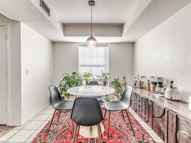 dining area with light tile patterned floors, baseboards, a raised ceiling, a textured wall, and a textured ceiling