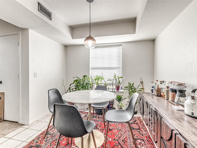 dining area with light tile patterned floors, visible vents, a raised ceiling, and a textured ceiling