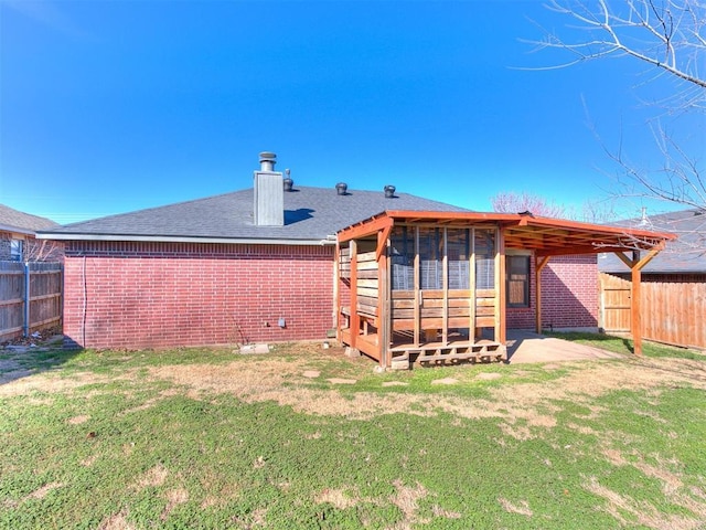 back of property with brick siding, a chimney, a shingled roof, a lawn, and fence