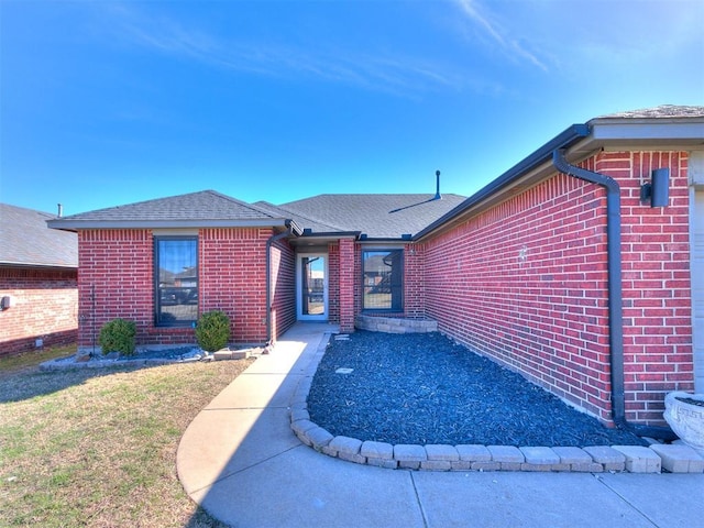 view of front of property featuring brick siding, a front lawn, and a shingled roof