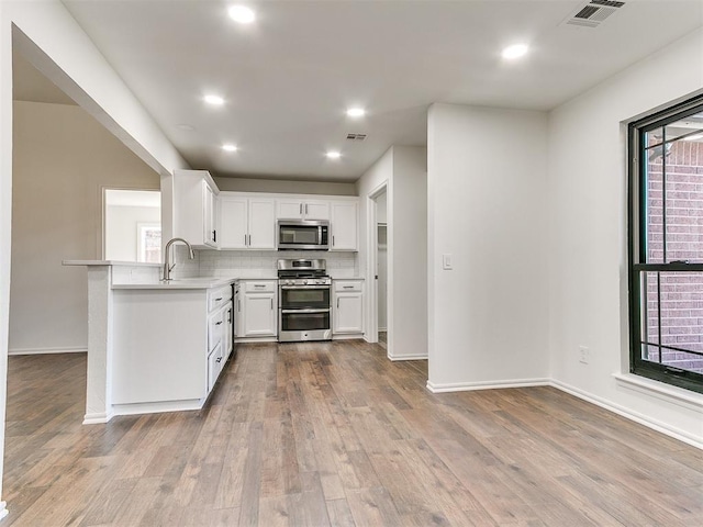 kitchen featuring stainless steel appliances, wood finished floors, visible vents, light countertops, and decorative backsplash