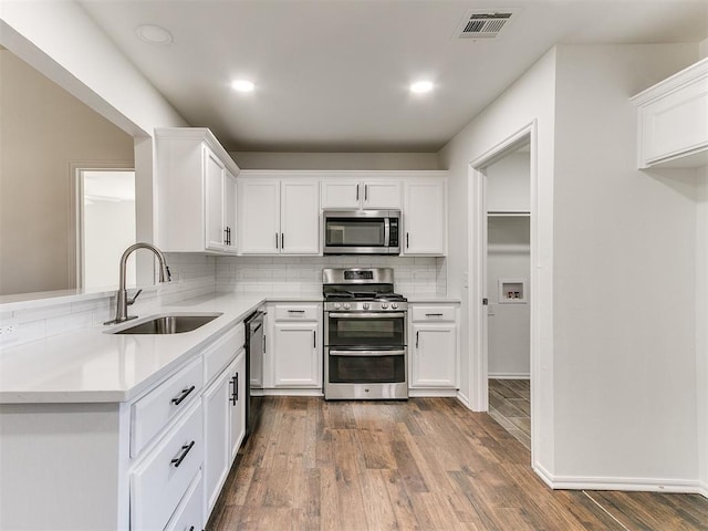 kitchen featuring dark wood-type flooring, a sink, visible vents, appliances with stainless steel finishes, and backsplash