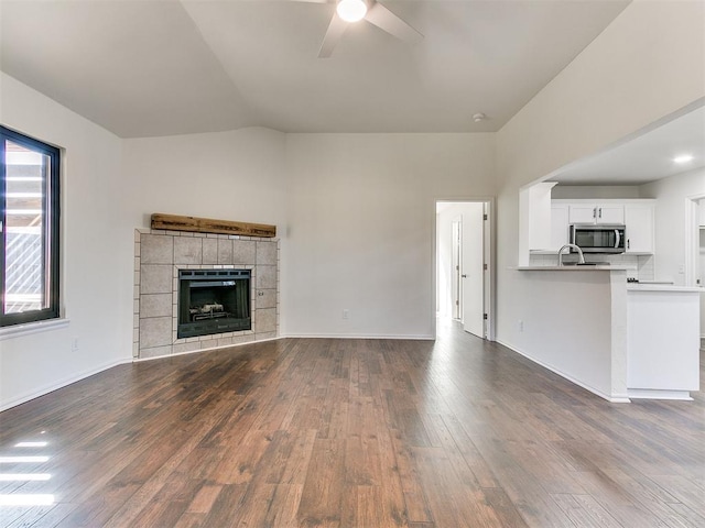 unfurnished living room with ceiling fan, a tile fireplace, dark wood-style flooring, baseboards, and vaulted ceiling