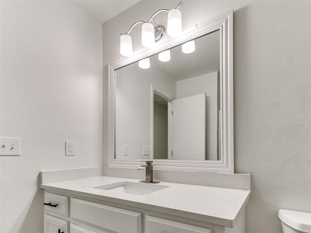 half bath with a textured wall, vanity, and toilet