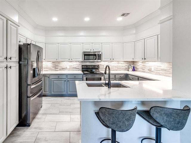 kitchen featuring appliances with stainless steel finishes, a breakfast bar, a peninsula, white cabinetry, and a sink