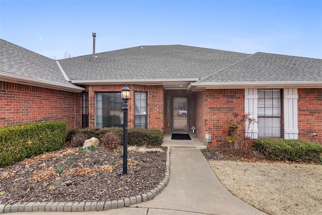 view of exterior entry with brick siding and roof with shingles