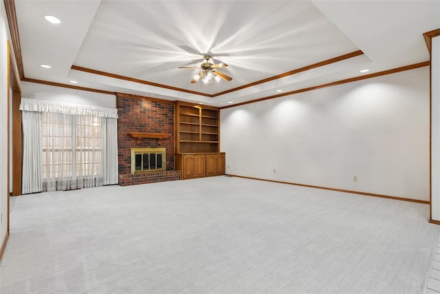 unfurnished living room featuring a raised ceiling, ornamental molding, a brick fireplace, carpet flooring, and baseboards