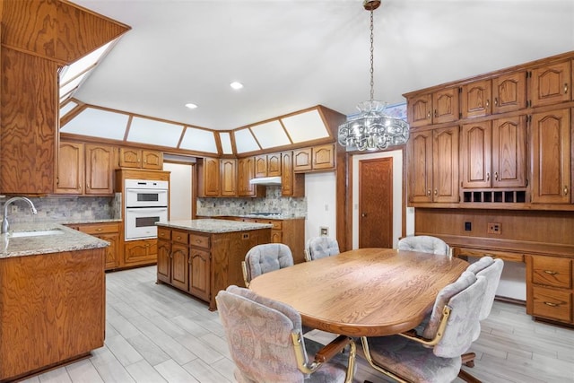 kitchen with brown cabinets, tasteful backsplash, double oven, a sink, and under cabinet range hood