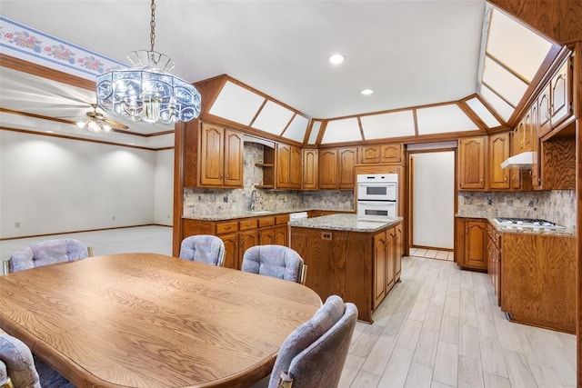 kitchen featuring an inviting chandelier, brown cabinetry, a sink, white appliances, and under cabinet range hood