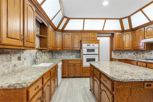 kitchen with lofted ceiling, light stone counters, white appliances, a sink, and brown cabinets