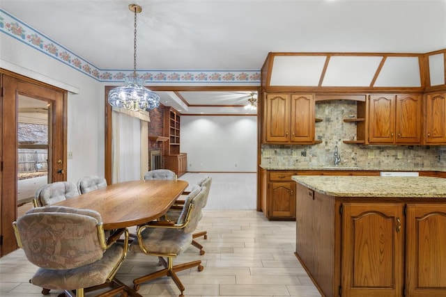 kitchen with light stone counters, a fireplace, backsplash, brown cabinetry, and decorative light fixtures