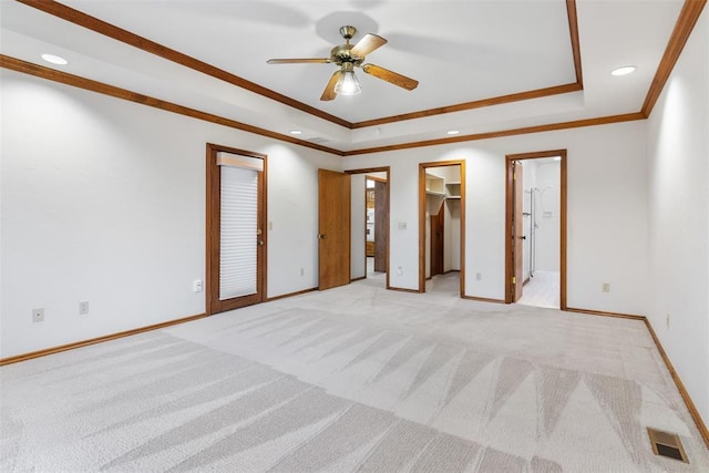 unfurnished bedroom featuring a raised ceiling, light colored carpet, visible vents, ornamental molding, and baseboards