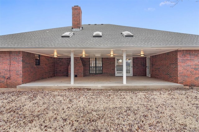 back of house with roof with shingles, brick siding, and a patio