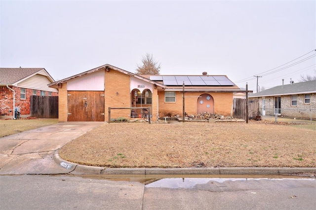 view of front of property featuring roof mounted solar panels, brick siding, fence, and driveway