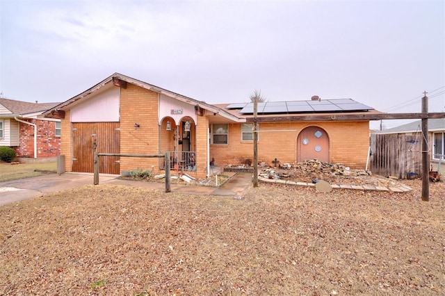 view of front of property featuring brick siding, fence, driveway, and solar panels