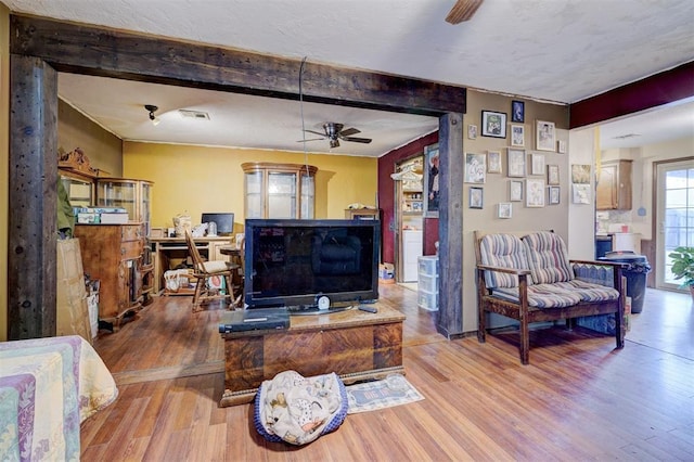 living area featuring visible vents, wood finished floors, beam ceiling, and a ceiling fan